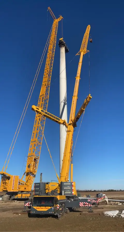 A crane is standing next to a wind turbine.